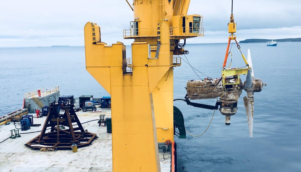 A turbine at the Meygen tidal power station in Scotland. A turbine hangs above the water in a crane from a ship.