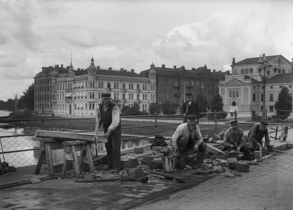 Svartvit bild där vägarbetare underhåller träkubben på Västra bron i Karlstad.