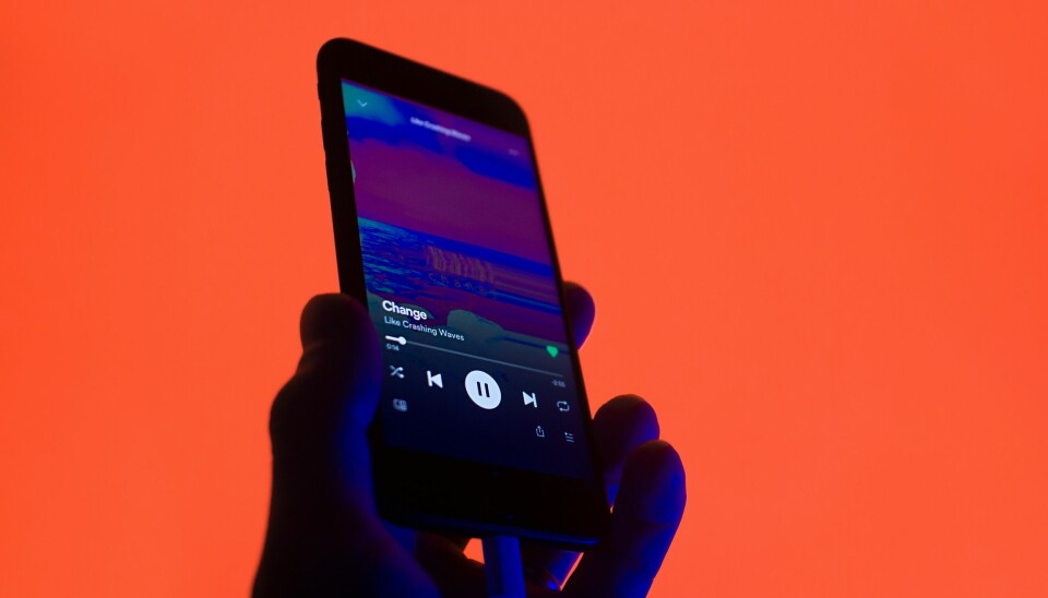 Hand som håller upp en telefon som spelar musik via Spotify, orange bakgrund