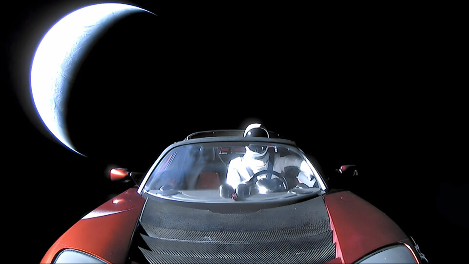 Dockan Starman på förarplats i en röd Tesla Roadster, fotograferad i rymden med en månskära i bakgrunden