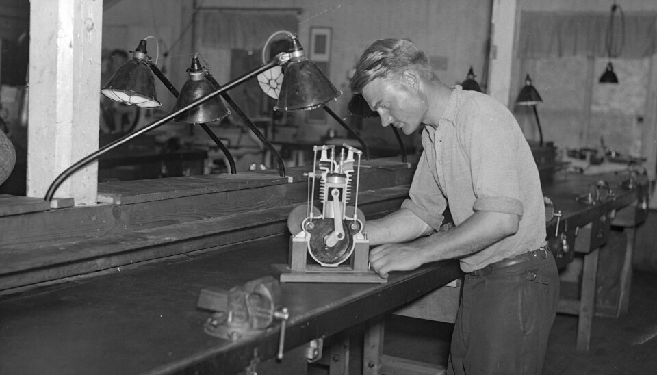 En man tittar på en modell som visar en tvåtaktsmotor i genomskärning. Den står på en hyvelbänk.