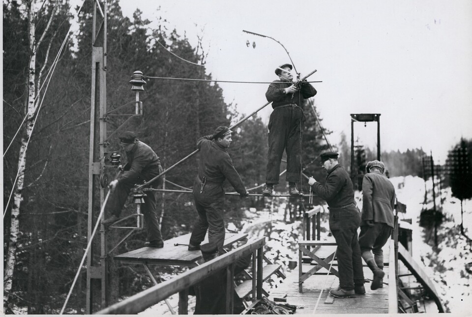 En grupp arbetsklädda män monterar ledningar till lok i ett vintrigt landskap.