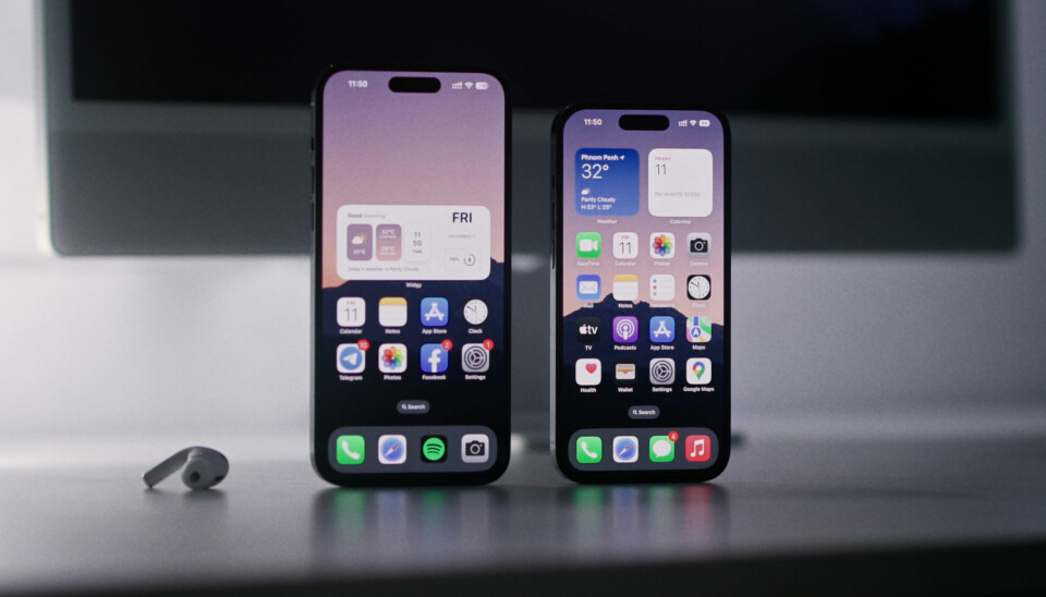 Bilden visar hemskärmen på två Iphone 14 Pro-modeller, stående på högkant på ett bord. Intill telefonerna ligger en Airpod-hörlur.