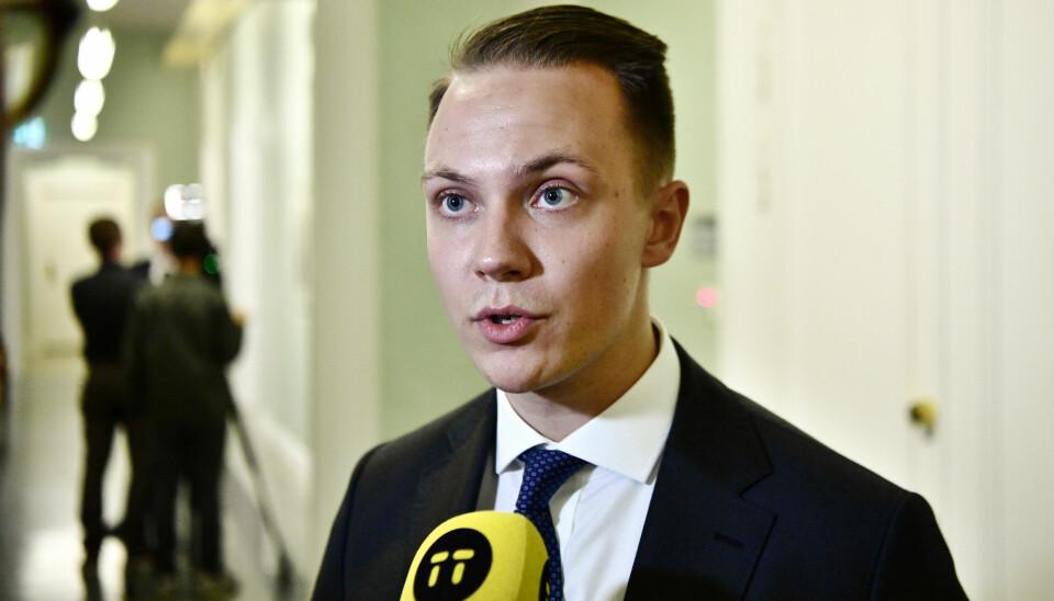 Tobias Andersson, SD, i svart, vit skjorta och svart slips. Han har en gul mikrofon framför sig