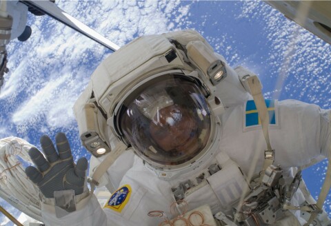 Astronauten Christer Fuglesang på rymdpromenad utanför rymdstationen ISS. Han vinkar mot kameran, i bakgrunden syns jorden.