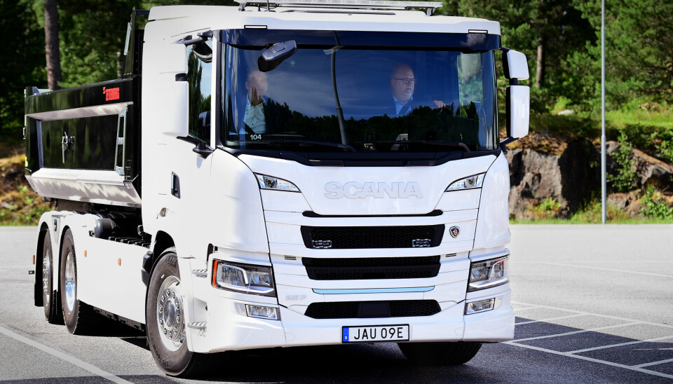 En vit lastbild från Scania som kör på asfalt. Bakom vita lastbilen syns grön natur.