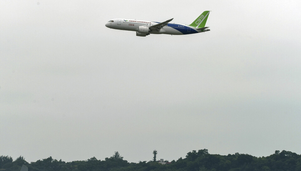Ett vit flygplan med blå och gröna detaljer i luften mot grå himmel