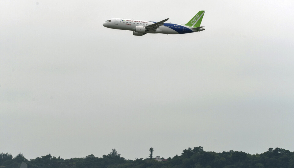Passagerarplanet C919 har testflugits många gånger. Arkivbild. Ett vit flygplan med blå och gröna detaljer i luften mot grå himmel