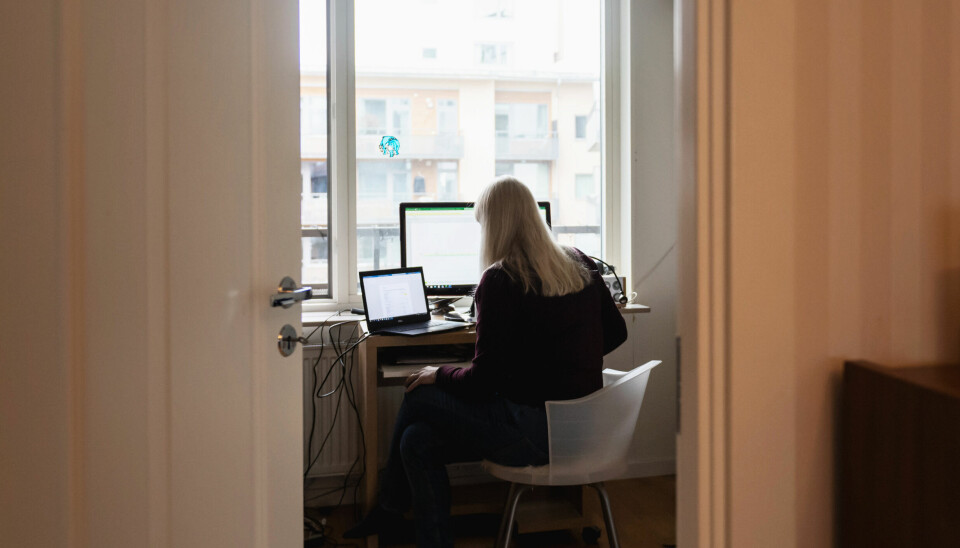 Ryggen på en kvinna som sitter och jobbar framför ett stort fönster och två datorskärmar.