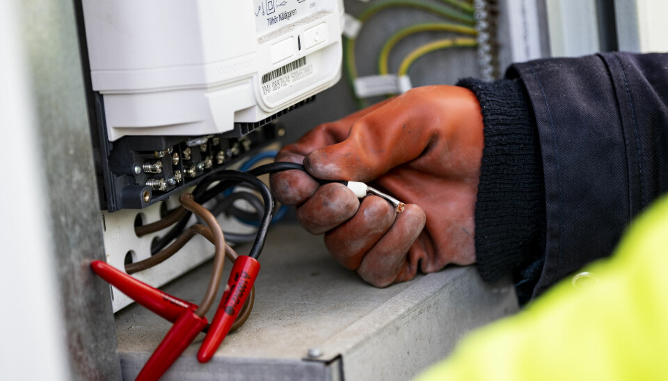 En elektriker med röd handske monterar ny elmätare. På några av sladdarna sitter röda detaljer