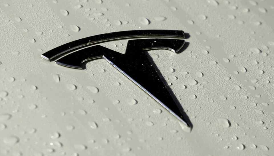 Fotot är en närbild av Teslas logotyp på huven av en elbil.