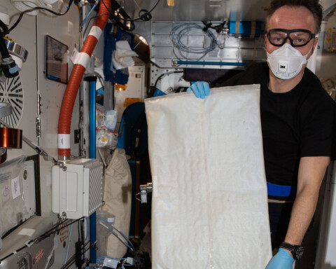 En astronaut håller upp en vit konstruktion på ISS.