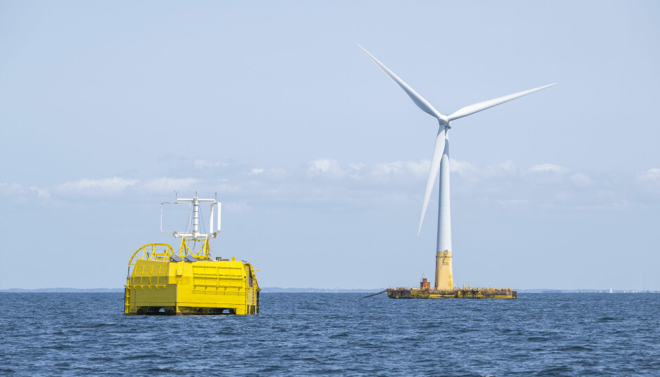 En gul pilotanläggning syns intill ett vindkraftverk i havet.
