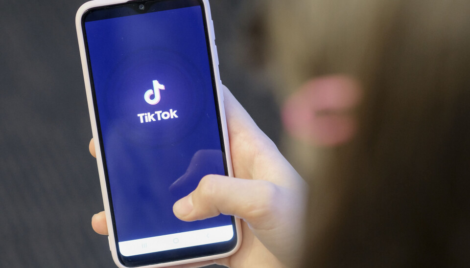 En hand som håller en mobiltelefon. Mobiltelefonen har en vit ram och på den syns texten TikTok