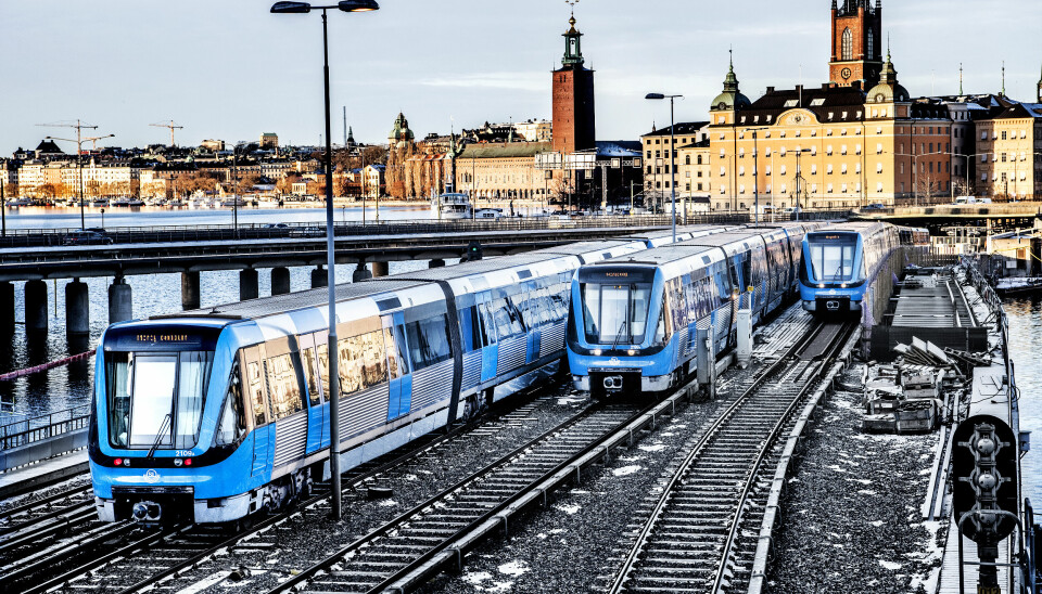 Gråa och blå tunnelbanetåg som rullar med en stadssilluet i bakgrunden