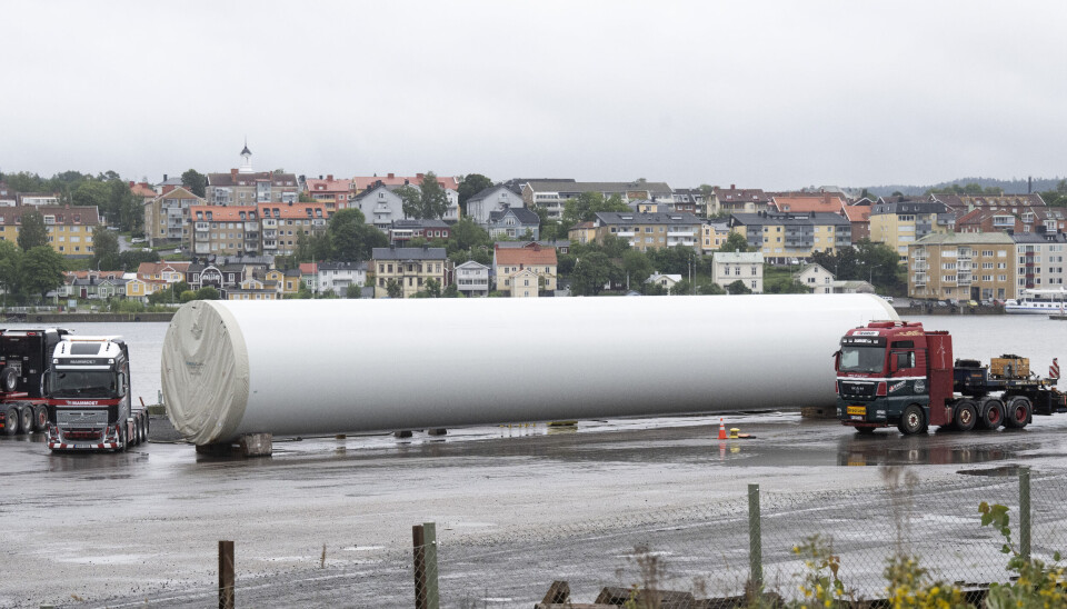 Nya fundament till vindkraftverk på väg. Arkivbild. Vitt stort cylinderformat fundament brevid en röd lastbil.