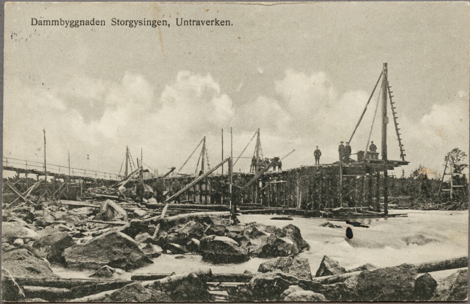 Arbetare bygger på dammen i Storgysingen, vattnet forsar mellan de stöttor som monterats fast