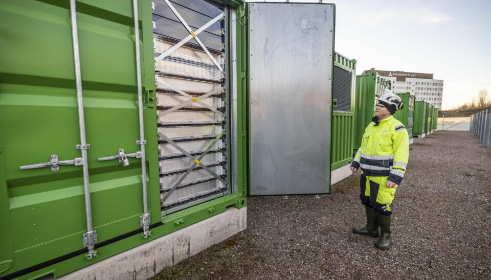 En man i varselkläder vid en grön battericontainer.