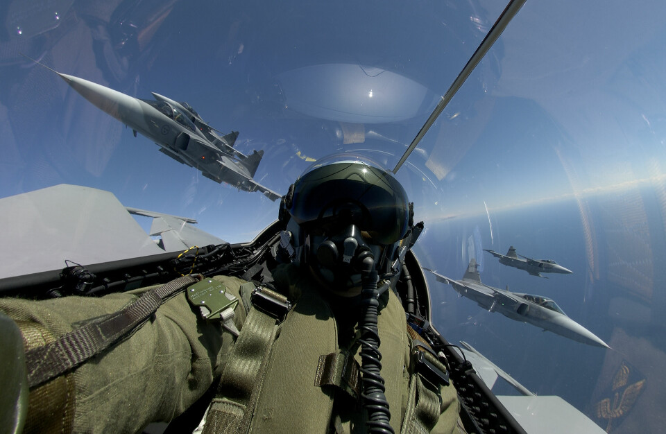 En stridspilot i en selfie tagen inne i cockpit under en flygning, utanför rutan syns tre ytterligare Jas Gripen