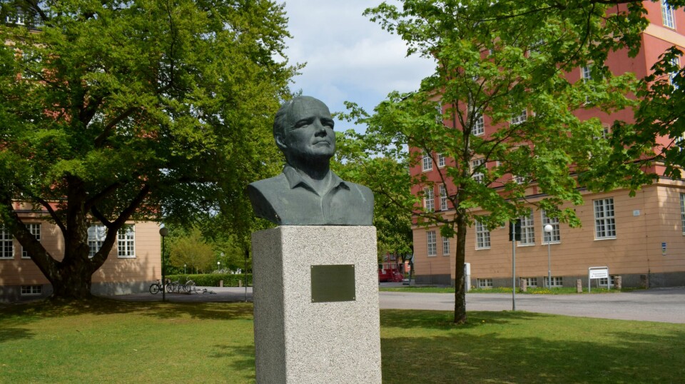 En bronsbyst föreställande Arne Beurling som står placerad på en gräsmatta med grönskande träd runt.