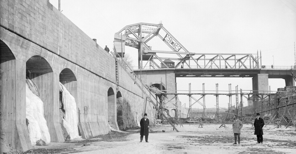Bilden visar den färdigställda Norra Danviksbron och Danvikskanalen under anläggande. Männen står på botten av den torrlagda Hammarby sjö.