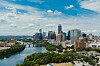 Panoramavy över Austins skyline med skyskrapor, grönskande parker och Colorado River under en blå himmel.
