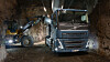 En blå Volvo-lastbil lastas av en gul hjullastare i en underjordisk tunnel eller gruva.