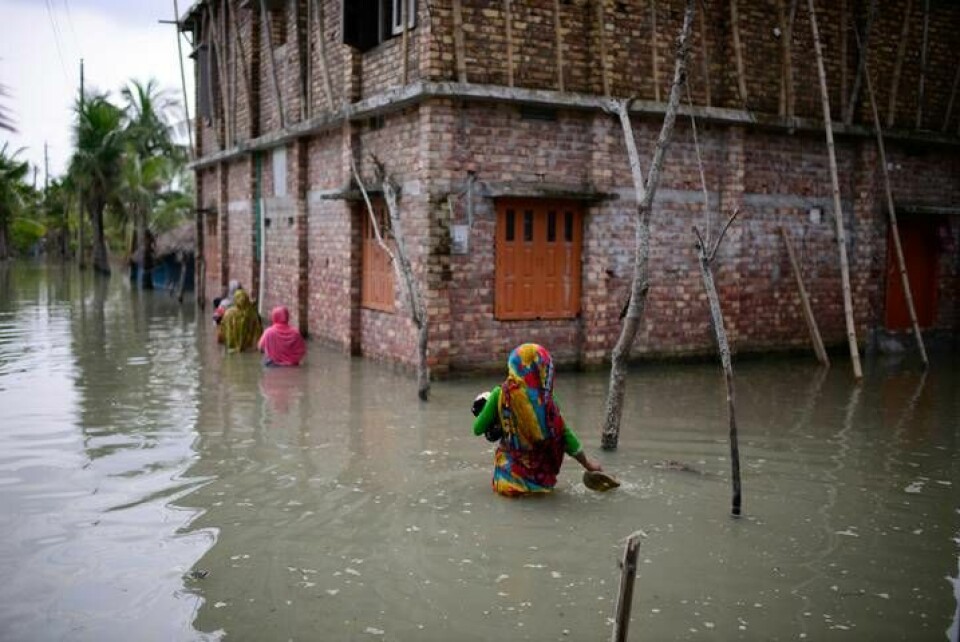 Invånare i byn Pratap Nagar i Bangladesh vadar genom vattenmassor för att ta sig till sina hem. Översvämningar blir vanligare i klimatförändringarnas spår. Arkivbild. Foto: Mahmud Hossain Opu/AP/TT