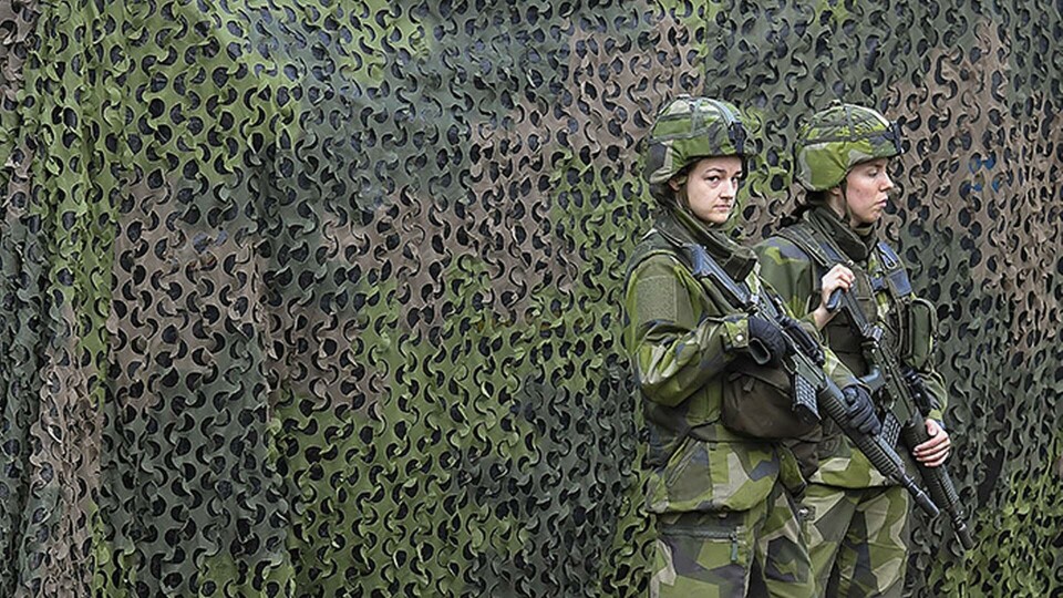 Militärfordon med skyddsnät vaktas av två soldater under försvarsövningen Aurora 17. Foto: Jonas Ekströmer / TT Militärfordon med skyddsnät vaktas av två soldater under försvarsövningen Aurora 17. Foto: Jonas Ekströmer / TT